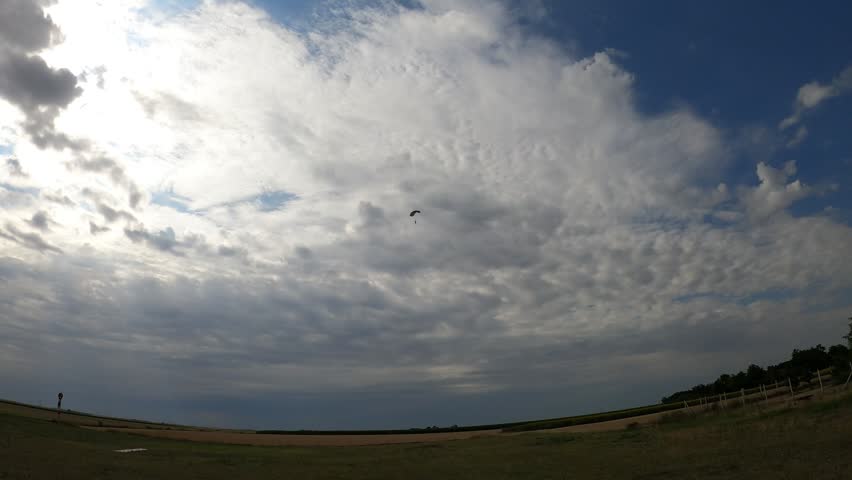 A skydiver with a gray parachute landing against a beautiful cloudy sky