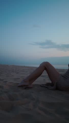 Bare legs resting on sandy beach at dusk with calm blue sky and soft horizon light