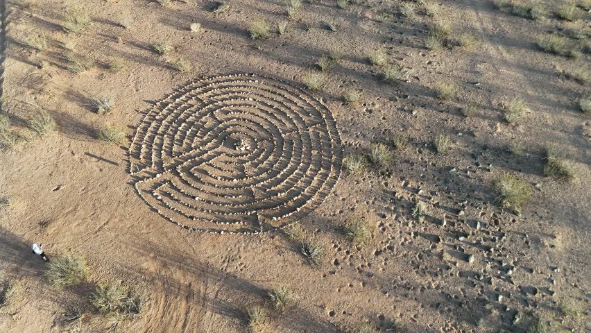 An aerial view of a circular stone labyrinth in the desert near St. George, Utah, USA surrounded by sand, dry vegetation, and long afternoon shadows.