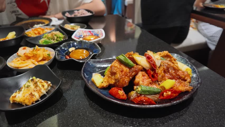 Close-up of wooden chopsticks lifting spicy fried chicken from a plate in Bangkok, Thailand.