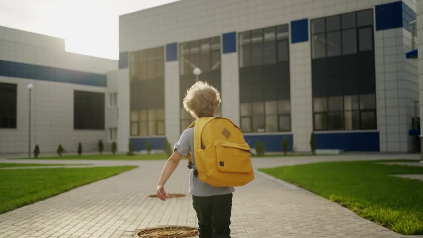 Happy elementary school students with backpacks walking together outside a school building on a sunny morning.