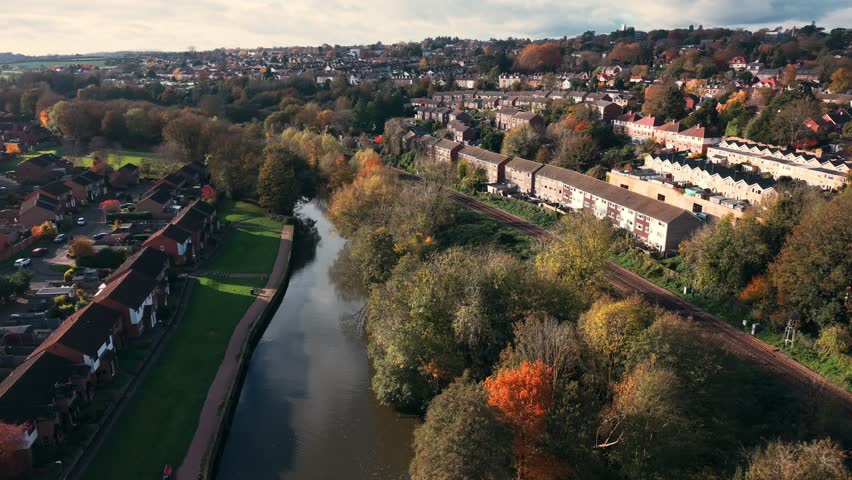An aerial view of the River Medway curving through Maidstone, Kent, with terraced housing, rail lines, and autumn trees under soft daylight
