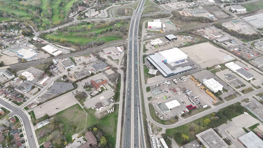 An aerial view of Ontario Highway 401 showing steady multilane traffic, commercial complexes, and green spaces under bright clear daylight