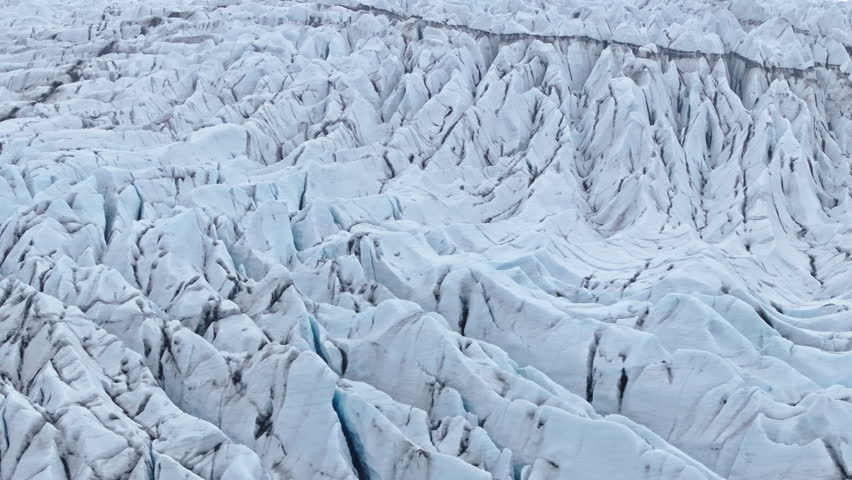 Abstract aerial view over textured glacier crevasses in Iceland. intricate pattern of jagged ice peaks and deep chasms. Melting glacial ice fields reveal dirty black ash stripes from ancient eruptions