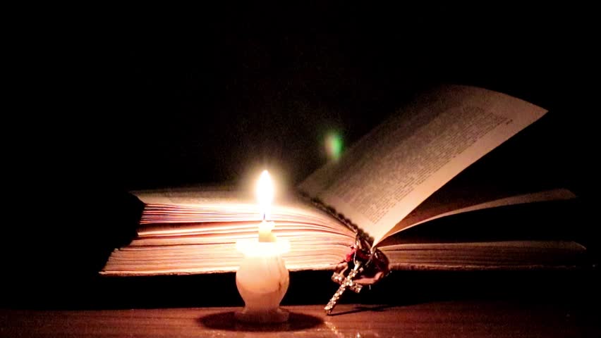 candle flame illuminates the pages of an old religious book