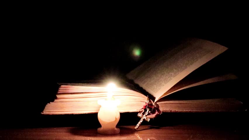 candle flame illuminates the pages of an old religious book