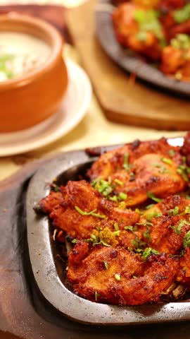Close-up of sizzling tandoori chicken and assorted Indian dishes served in a Bangkok restaurant.