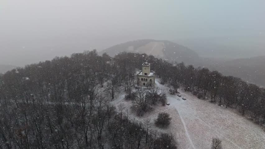 Visegrád, Hungary, Zsitvay-kilátó observation tower on a snowy hilltop in the Visegrád Mountains, surrounded by bare forest trees during winter weather, aerial view.