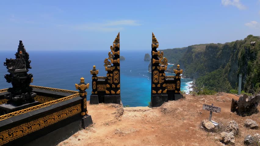 Aerial drone view through iconic Balinese gate overlooking dramatic limestone cliffs and turquoise ocean on Nusa Penida Island, Bali, Indonesia. Scenic tropical coastline and famous travel destination