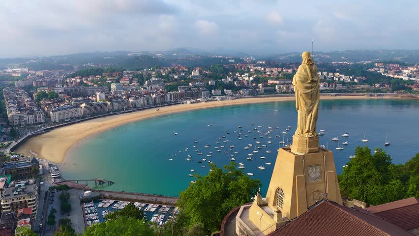 Morning aerial view of San Sebastián city in Basque Country, northern Spain. Orbiting drone shot of Jesus Christ statue in San Sebastián old town, vacation in Basque Country