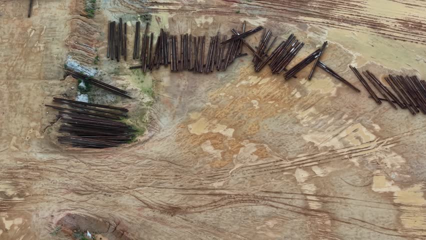 Aerial of a logging site showing stacked construction material and dirt tracks in a forested rural area with natural earth tones and tree cover.