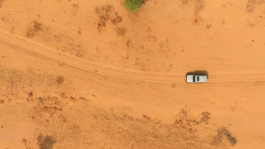 Top-down drone view of a vehicle driving on a sandy track through the Thar Desert in Sindh, Pakistan, with tire marks and dry scrub.
