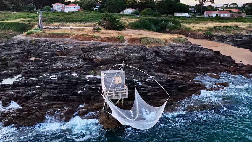 Aerial view of a traditional wooden fishing hut with a large net suspended over the rocky coastline in Nantes, Pays de la Loire, France.
