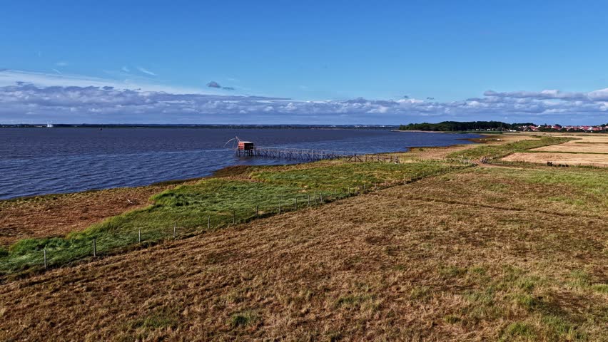 Aerial view of a traditional fishing hut on the Garonne river with grassy banks and calm water in Bordeaux, Nouvelle-Aquitaine, France.