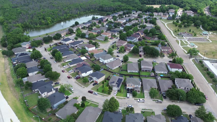 Suburban residential streets wrap around stormwater retention pond near Trinity River greenbelt. Single family homes with gray shingle roofs border neighborhood park spaces, Dallas, Texas. USA