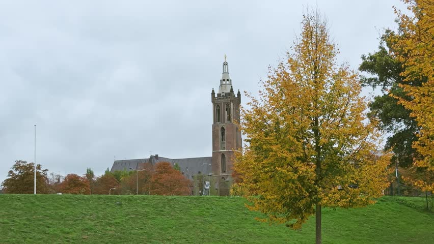 St Christophers Cathedral, a historic Gothic church in Roermond, Netherlands, stands under an overcast sky. Vibrant autumn foliage surrounds this iconic landmark, showcasing centuries of European architectural heritage.