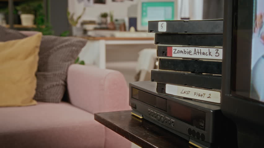 Retro VHS tapes sitting stacked on VCR player next to flickering CRT television in living room. Ideal for retro marketing, vintage media documentaries, or 90s themed commercial projects