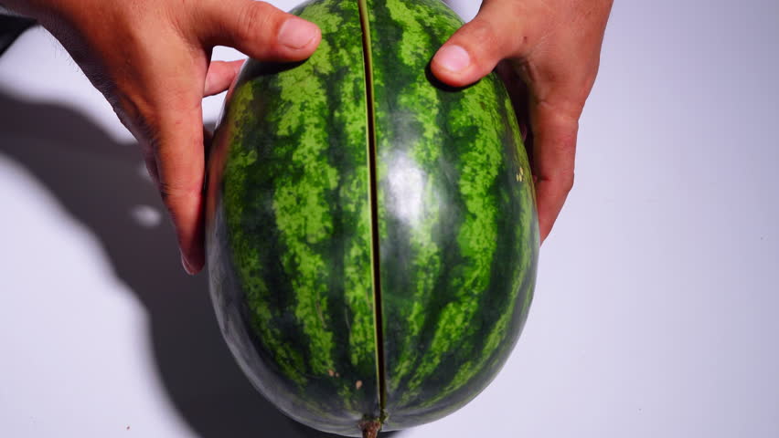 Opening a cut watermelon to reveal the appetizing red flesh inside.