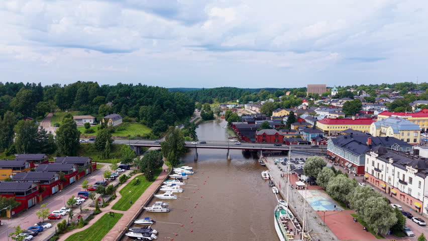 Aerial view over Porvoonjoki river toward Porvoo old town, showing colorful traditional wooden houses, road bridge, moored boats along the quay, and church tower, Finland