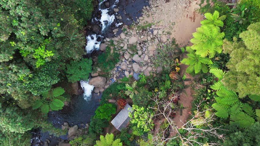 Aerial view of a waterfall cascading through basalt columns. Water plunges into a deep, narrow gorge. Rugged, jagged cliffs frame the falling stream. Exposed earth and stone surround the dramatic drop