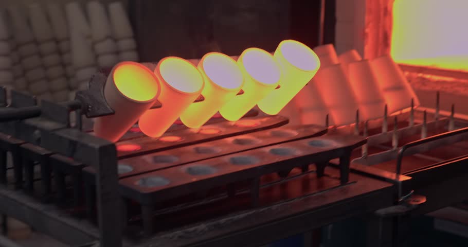 Slow motion close up of molten gold, copper metal pouring from crucibles into molds inside industrial foundry near glowing furnace in Concentration factory.