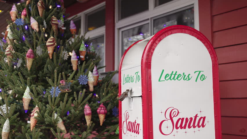 An Asian boy approaches a red and white Santa mailbox and drops his Christmas letter inside.