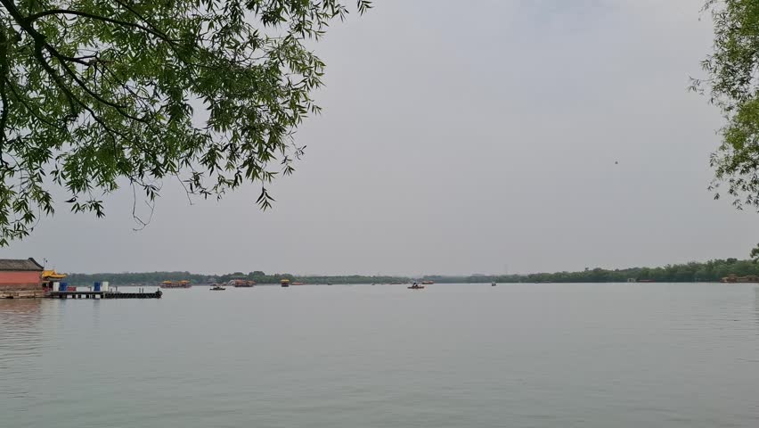 Traditional boats float on Kunming Lake under an overcast sky at Summer Palace. Beijing travel, Chinese heritage site, scenic water landscape. peaceful moment, relaxation, escape.