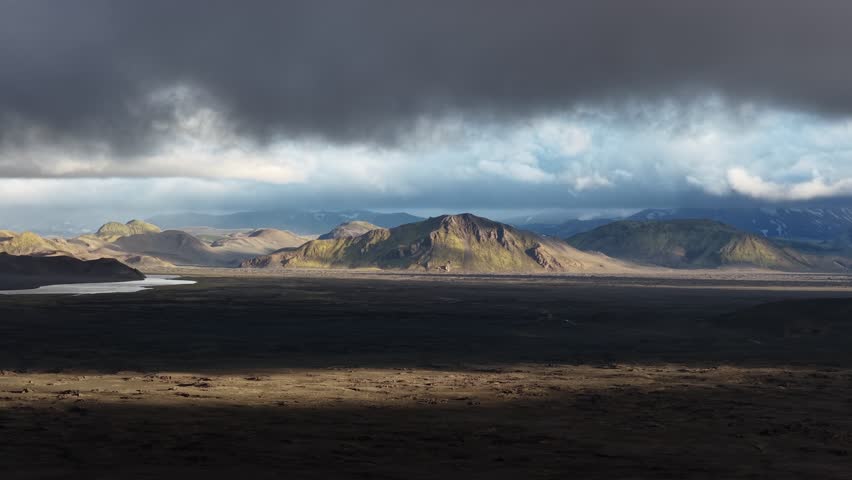Aerial view of Landmannalaugar volcanic landscape with mossy green mountains and dramatic storm clouds over the rugged terrain in Rangarthing ytra, Iceland.
