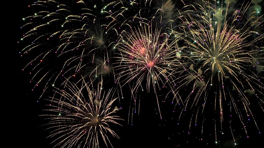 Bright sparks of fireworks in the night sky, purple and gold. Medium shot