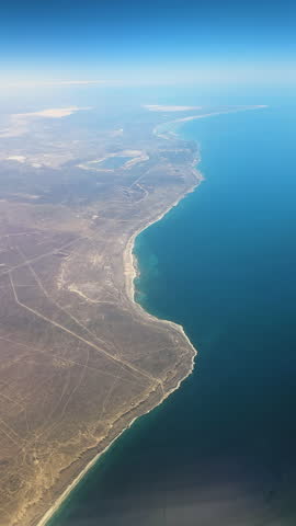Scenic aerial view flying over vast desert terrain meeting the deep blue ocean water along a dramatic and beautiful coastline with clear skies extending to the horizon