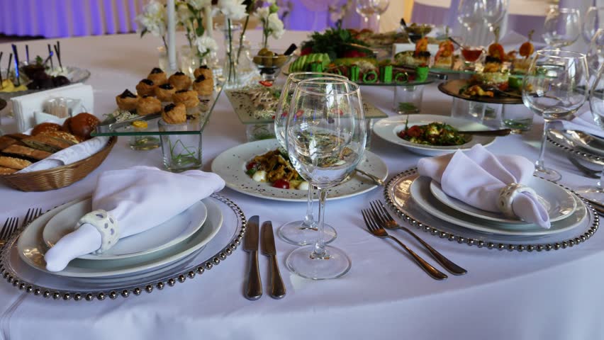 Elegant wedding banquet table setting with white napkins, wine glasses and gourmet catering food.