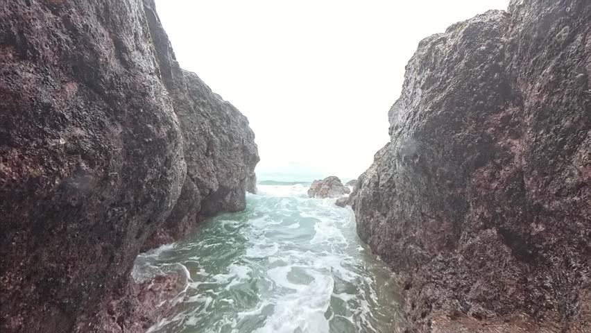 Powerful ocean waves crashing between dark rocky cliffs with sea spray