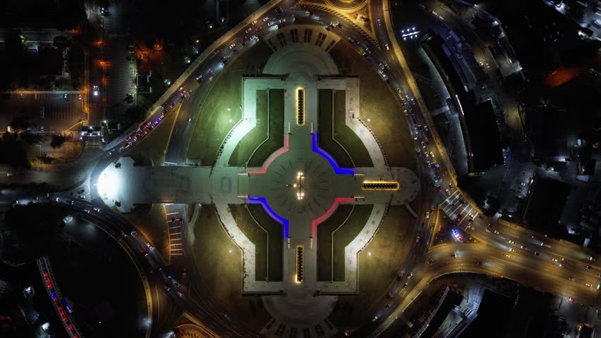 Aerial view of the illuminated Plaza de la Bandera monument surrounded by city traffic and urban lights in Santo Domingo, Santo Domingo Provinc, Dominican Republic.