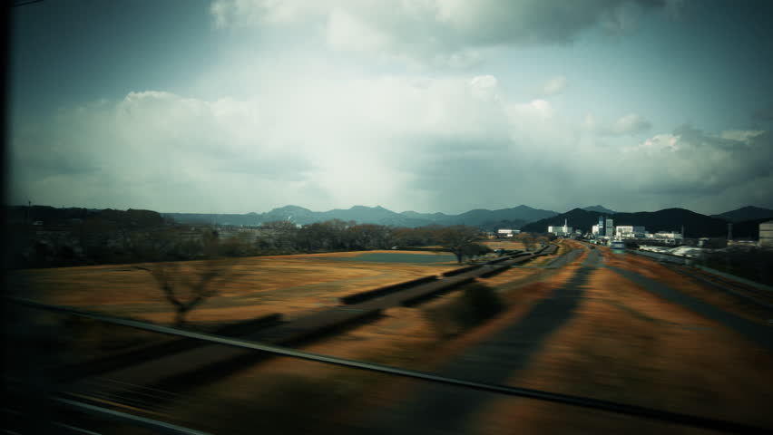 View Through a Shinkansen Bullet Train Window as a Wide Riverbed, Mountains and Dramatic Storm Clouds Rush Past at High Speed in Japan