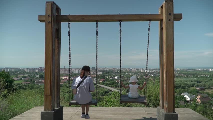 Tourist spot, swing with panoramic view, two girls riding, slow motion, sunny summer day