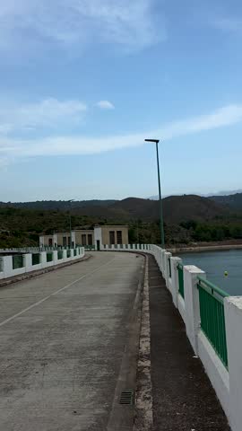 View of Beniarres reservoir lake from dam bridge with yellow safety buoys line, smooth water surface and mountain range in background, Alicante, Spain.Vertical 4K 