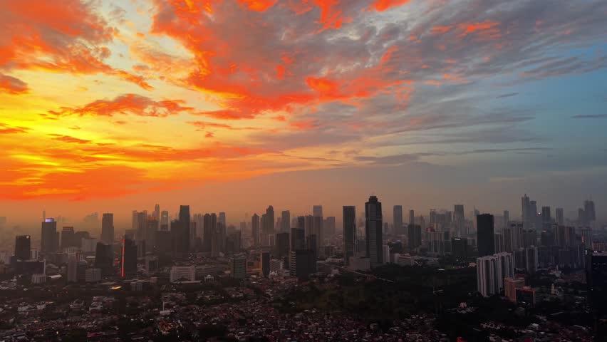 Aerial view of the vibrant Jakarta skyline illuminated by a dramatic orange sunset, showcasing urban architecture and high-rise buildings in Tebet, Jakarta, Indonesia.