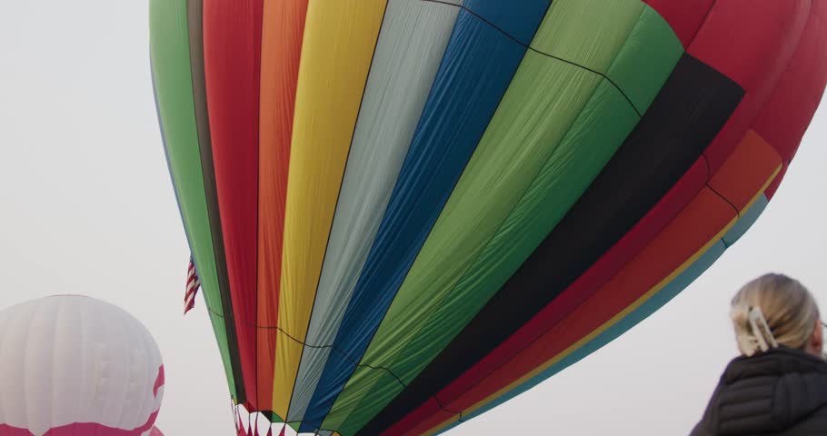 A colorful hot air balloon lifts into the sky as people watch from below during a morning launch event