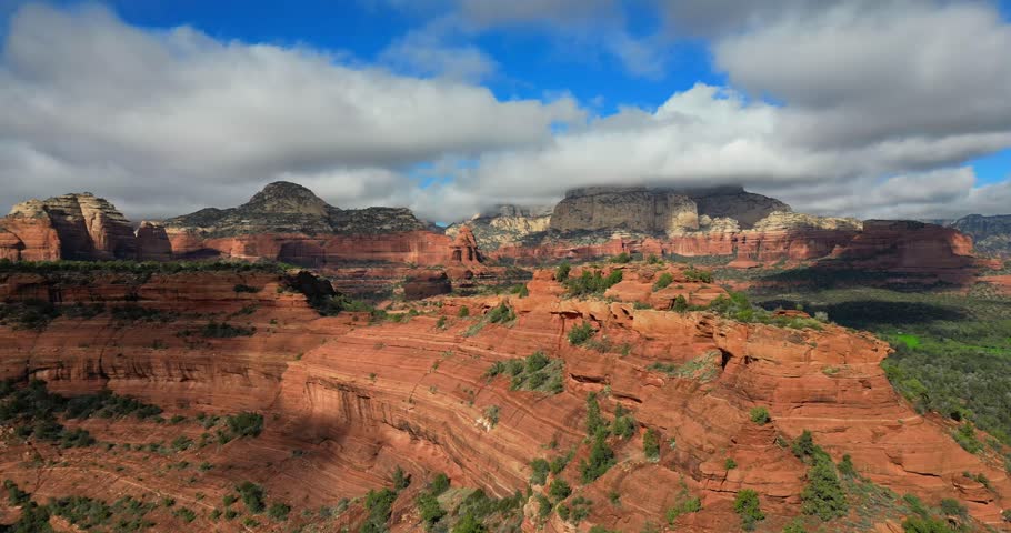 An aerial view of the expansive red rock formations of Red Rock State Park, layered cliffs stretching beneath soft clouds across the Sedona landscape