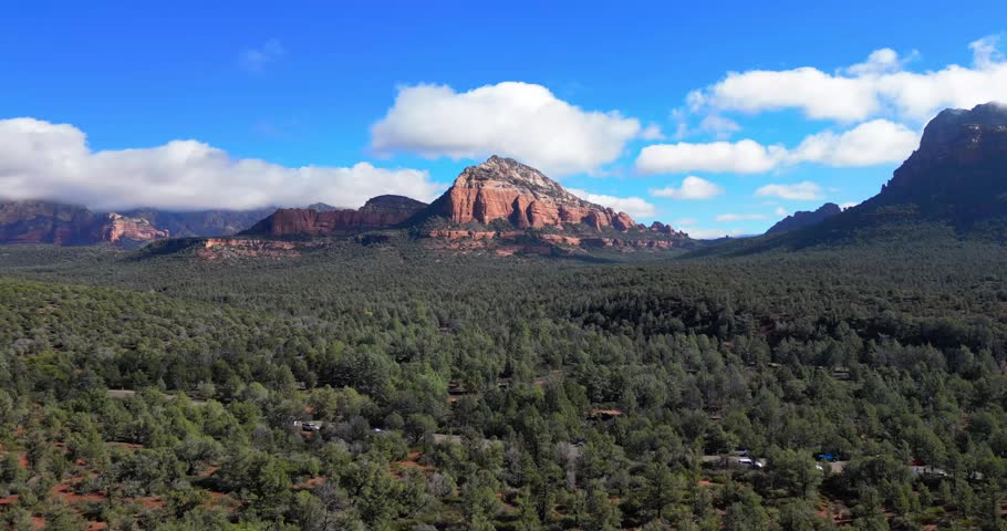 A rising drone view lifting above forested valleys toward Sedona