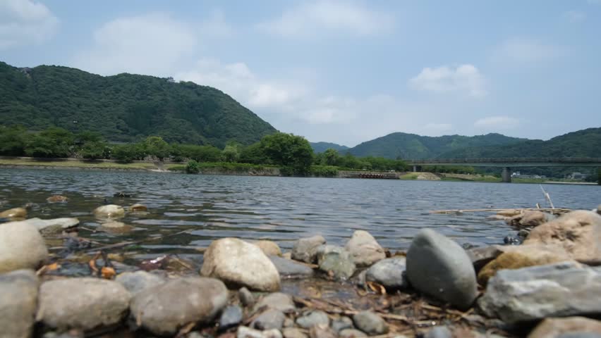 Gentle River Ripples Flowing Toward a Rocky Shore with Mountain Scenery