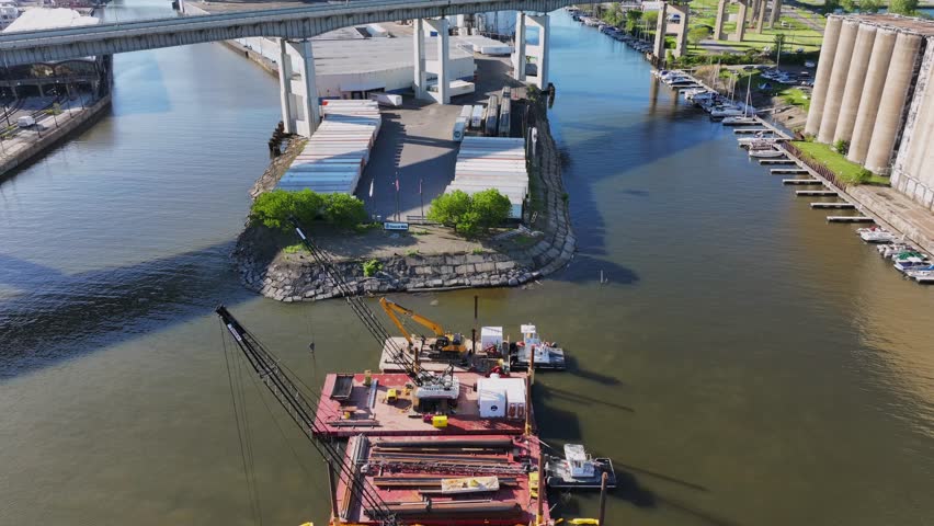 Aerial view of crew teams rowing under the Buffalo Skyway past construction barges and industrial grain silos on the Buffalo River in Buffalo, New York, United States.