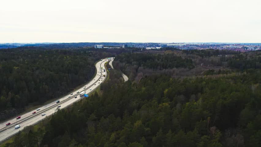 Aerial drone view of National Road 40 passing through Delsjo forest with moving traffic and dense woodland near Gothenburg Sweden during daytime