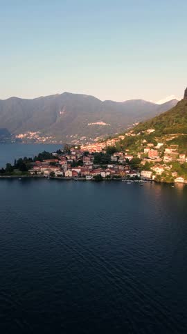 Aerial view of the village of Torno on the shores of Lake Como, with historic stone buildings and lush green hillsides reflecting in the water, Torno, Lombardy, Italy.