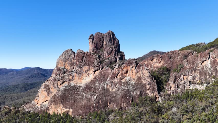 Wide shot of ancient volcanic rock formations under a clear blue sky in Warrumbungle, Australia.