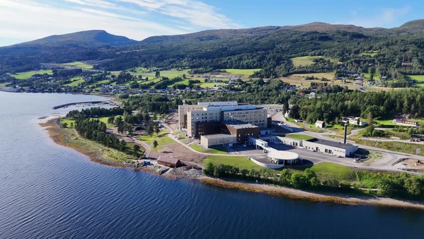 An aerial view of the new built Nordmoere and Romsdal Hospital at Hjelset with green hills, sea and parking lot in Molde municipality, Norway.