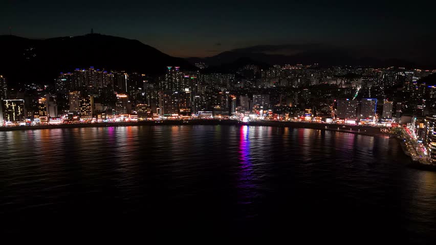 Aerial view of Gwangalli Beach at night with illuminated city skyline reflecting on the dark water of the bay in Busan, Busan, South Korea.