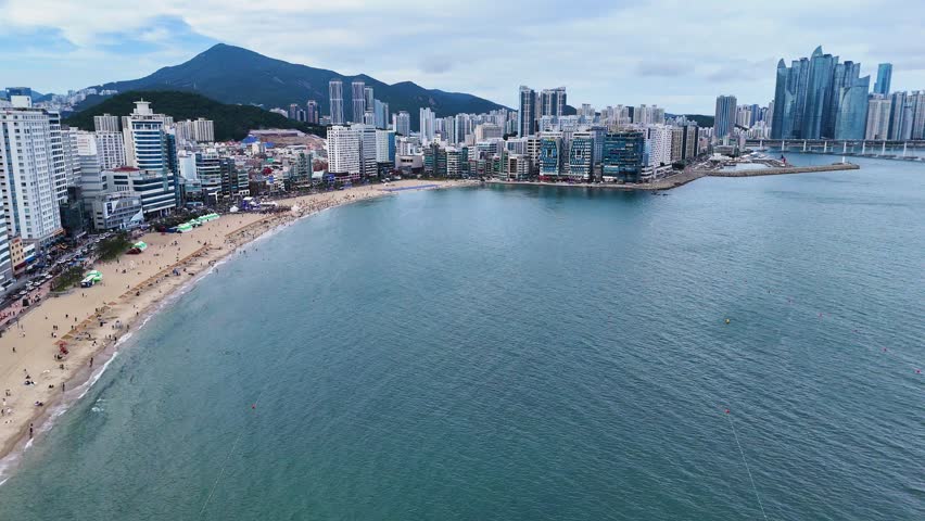Aerial view of Gwangalli Beach with sandy shore, urban skyline, and modern skyscrapers along the coastline in Busan, Busan, South Korea.