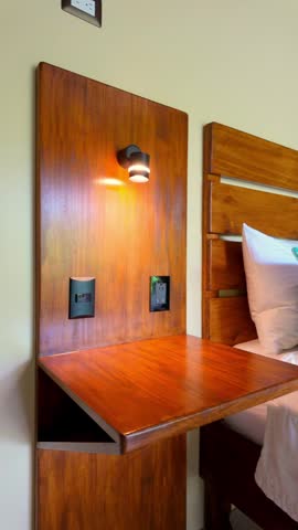 Comfortable and cozy hotel bedroom interior revealing a freshly made bed with white sheets and vibrant turquoise pillows, complemented by warm lighting and a modern wooden headboard