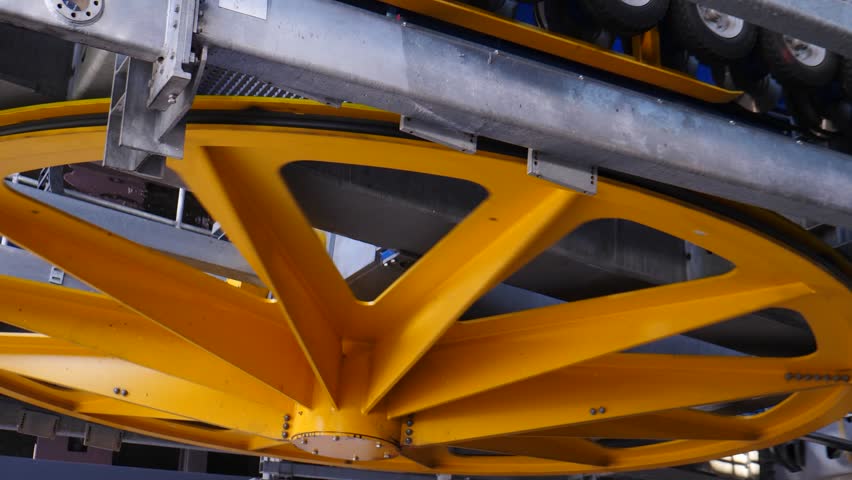 Low-angle close-up of a massive yellow six-spoke metal sheave wheel for a cable car station, mounted beneath a steel beam with guide rollers for the rope system 4k video